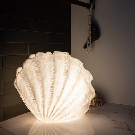 Extra large Clam Shell Reef Lamp glowing on a marble shelf in a coastal interior