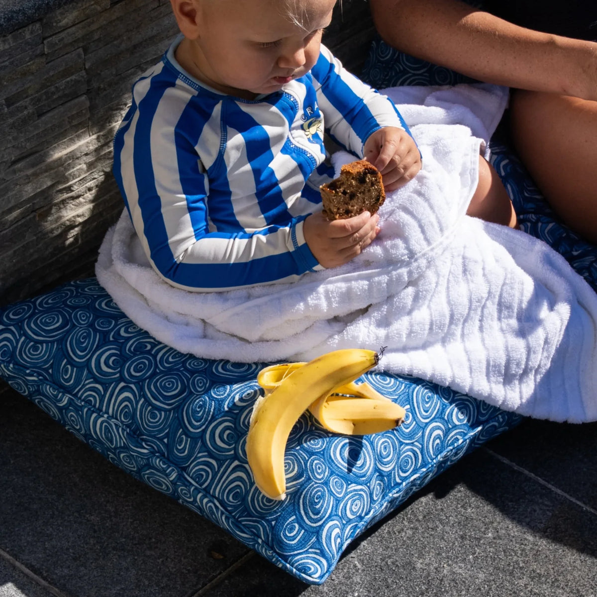 Ocean Growth Rings outdoor indoor cushion cover in blue used for relaxed poolside seating with a baby and white towel.