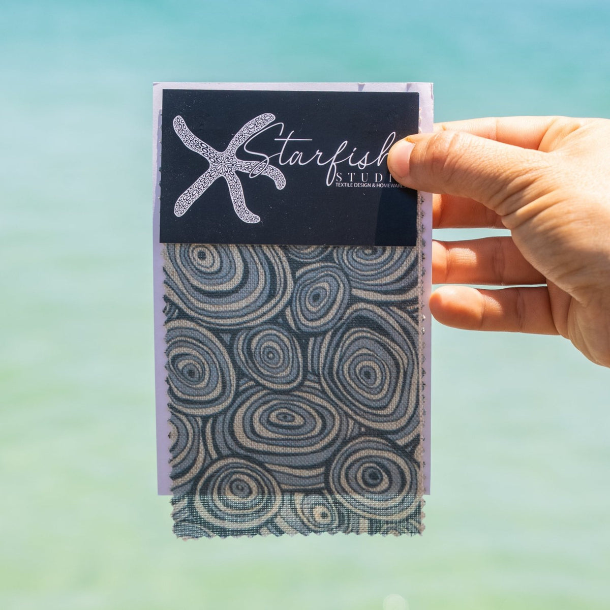 Frenchmans Growth Rings linen fabric swatch in blue and natural tones held against a coastal background