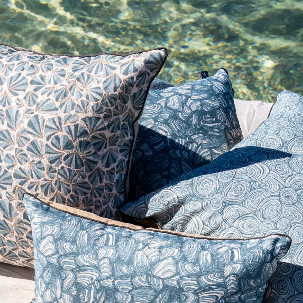 Frenchmans Pipi linen cushion cover styled outdoors with matching Starfish Studio cushions beside the water.