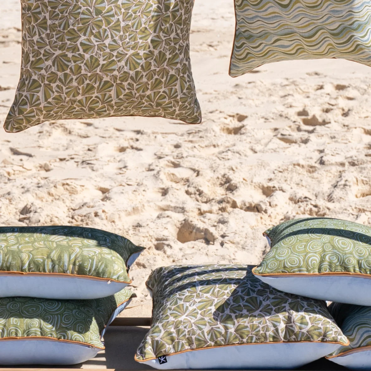 Starfish Studio coastal linen cushion collection displayed on the beach with green Pipi, Growth Rings, Shells and Straddie Stripe designs.