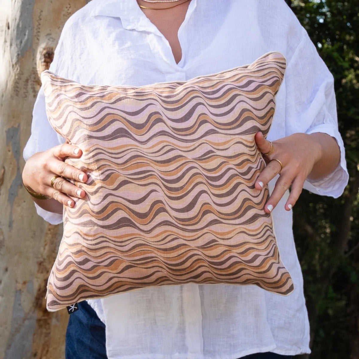 Woman holding square Claytons Straddie Stripe linen cushion cover in soft earthy tones