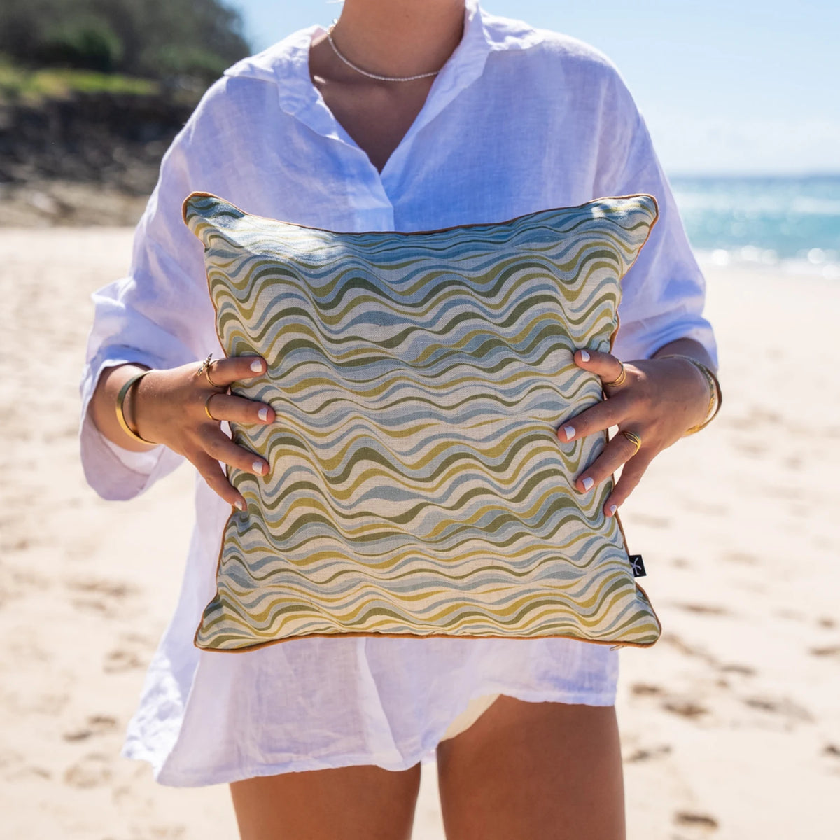 Woman holding Straddie Stripe linen cushion cover in green and blue coastal tones at the beach