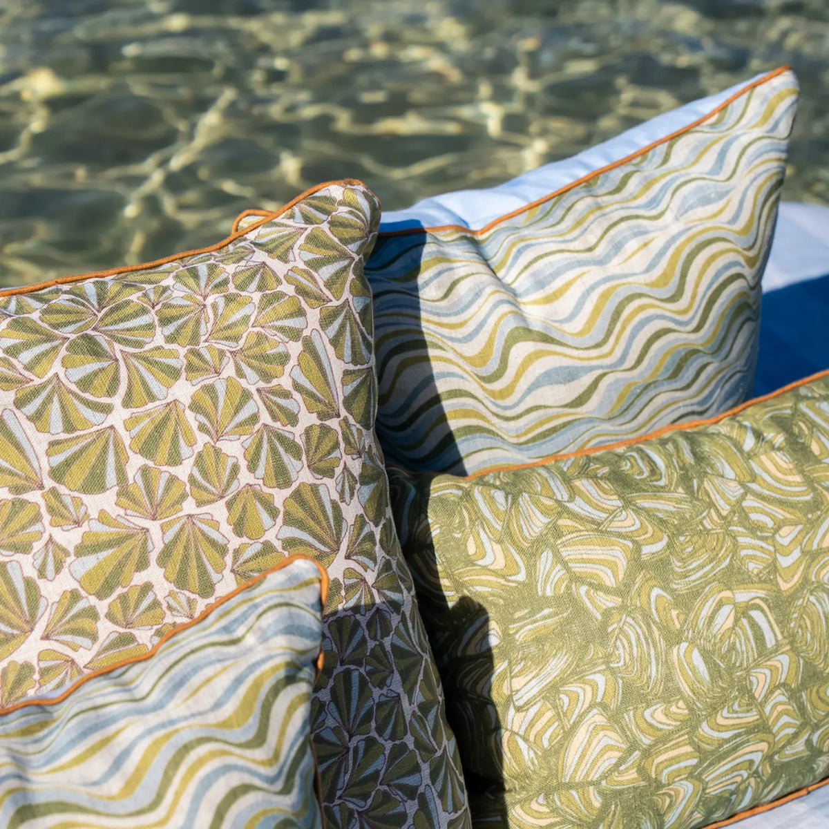 Mangrove linen cushion covers in coordinating coastal prints styled together beside the water