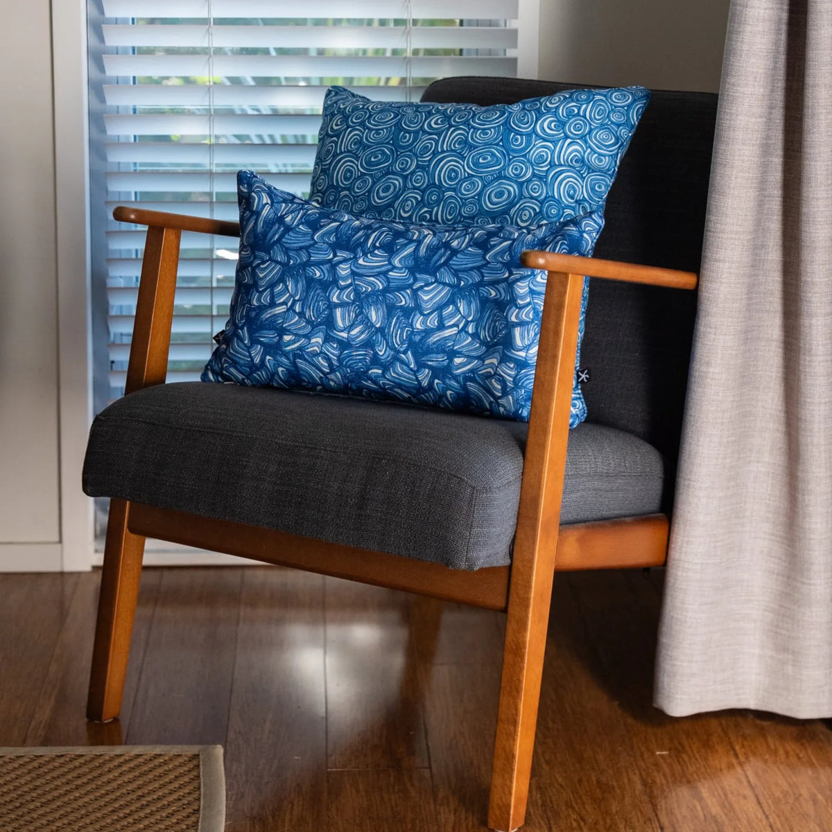Pacific cushions styled on a charcoal armchair indoors with a square Growth Rings cushion and a Pipi lumbar cushion.