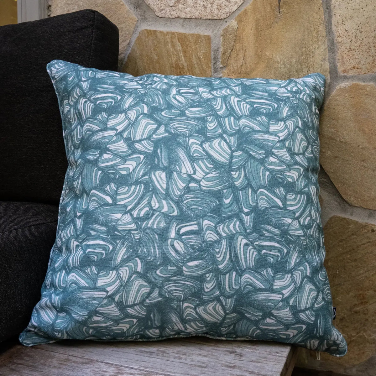 Square outdoor and indoor cushion in the Frenchmans colourway featuring the Pipi pattern, styled on a timber chair beside a stone wall.