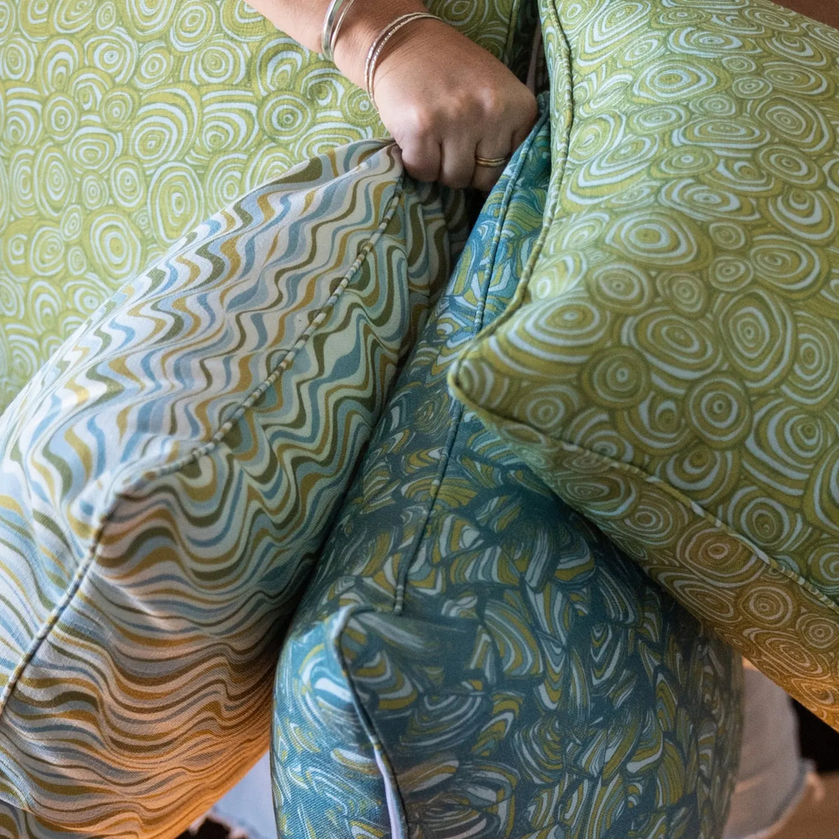 Close-up of Mangrove cushions in Pipi, Growth Rings and Straddie Stripe prints being held together.