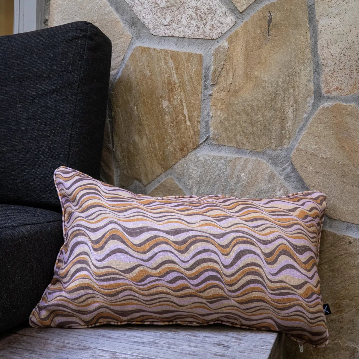 Claytons Straddie Stripe outdoor indoor cushion cover in a rectangular lumbar size styled on an outdoor chair beside a stone wall.