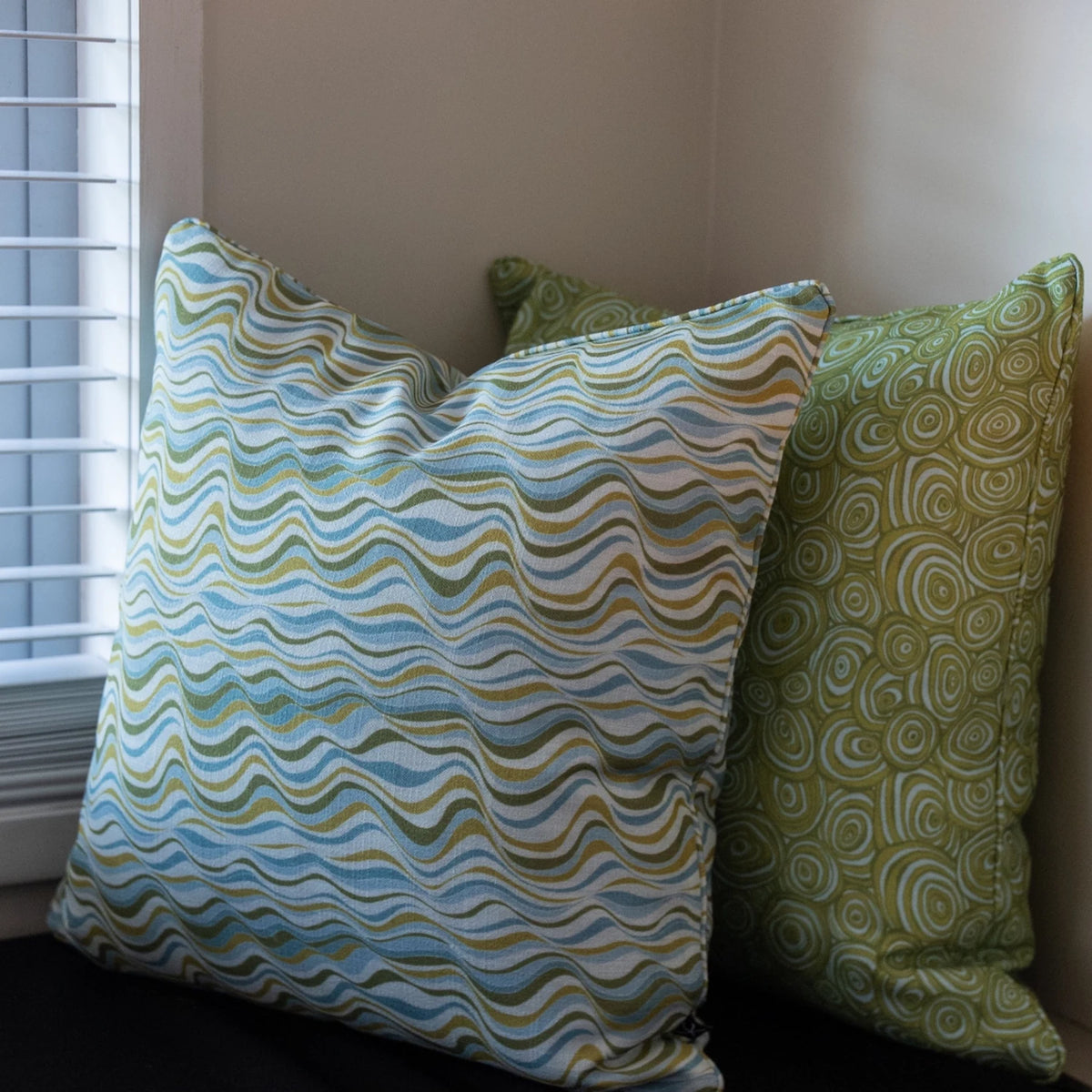 Mangrove Straddie Stripe outdoor indoor cushion covers styled beside coordinating Growth Rings cushions near a window.
