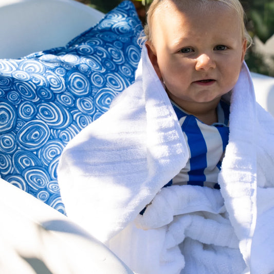 Ocean Growth Rings outdoor indoor cushion cover in blue styled behind a baby wrapped in a white towel by the pool.