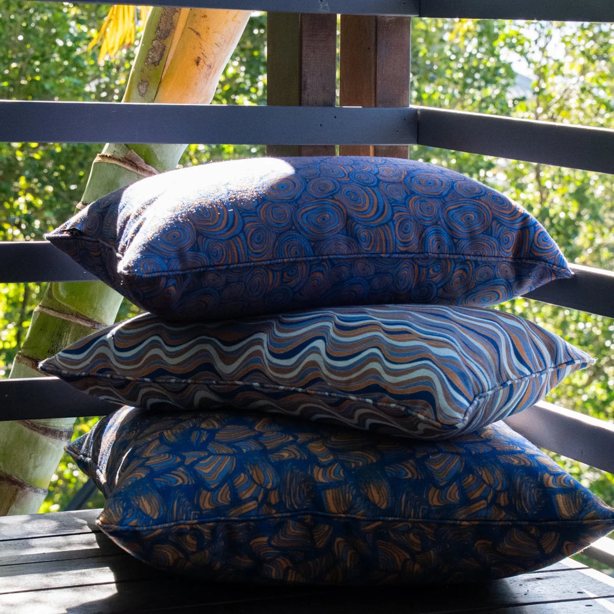Stack of three outdoor cushions showing circular, wavy and abstract blue-toned prints.