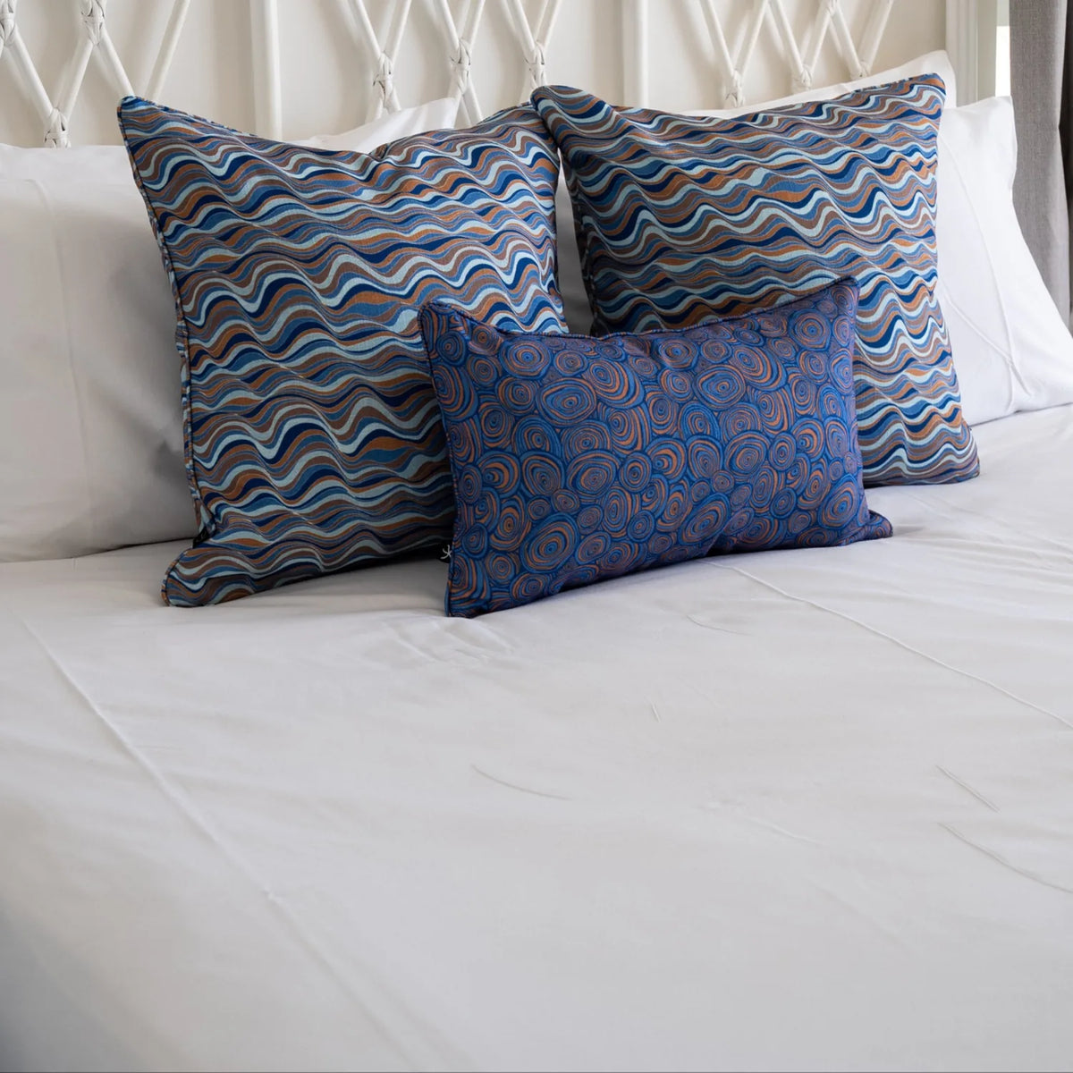 Bedroom styling with two large patterned square cushions and one matching lumbar cushion on a white bed.
